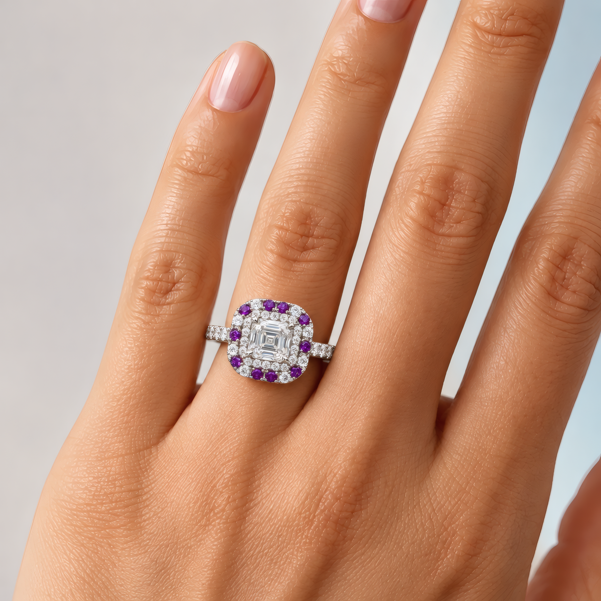 Kea engagement ring in white gold worn on a woman's hand, showing the Asscher-cut diamond in a double halo of diamonds and purple stones
