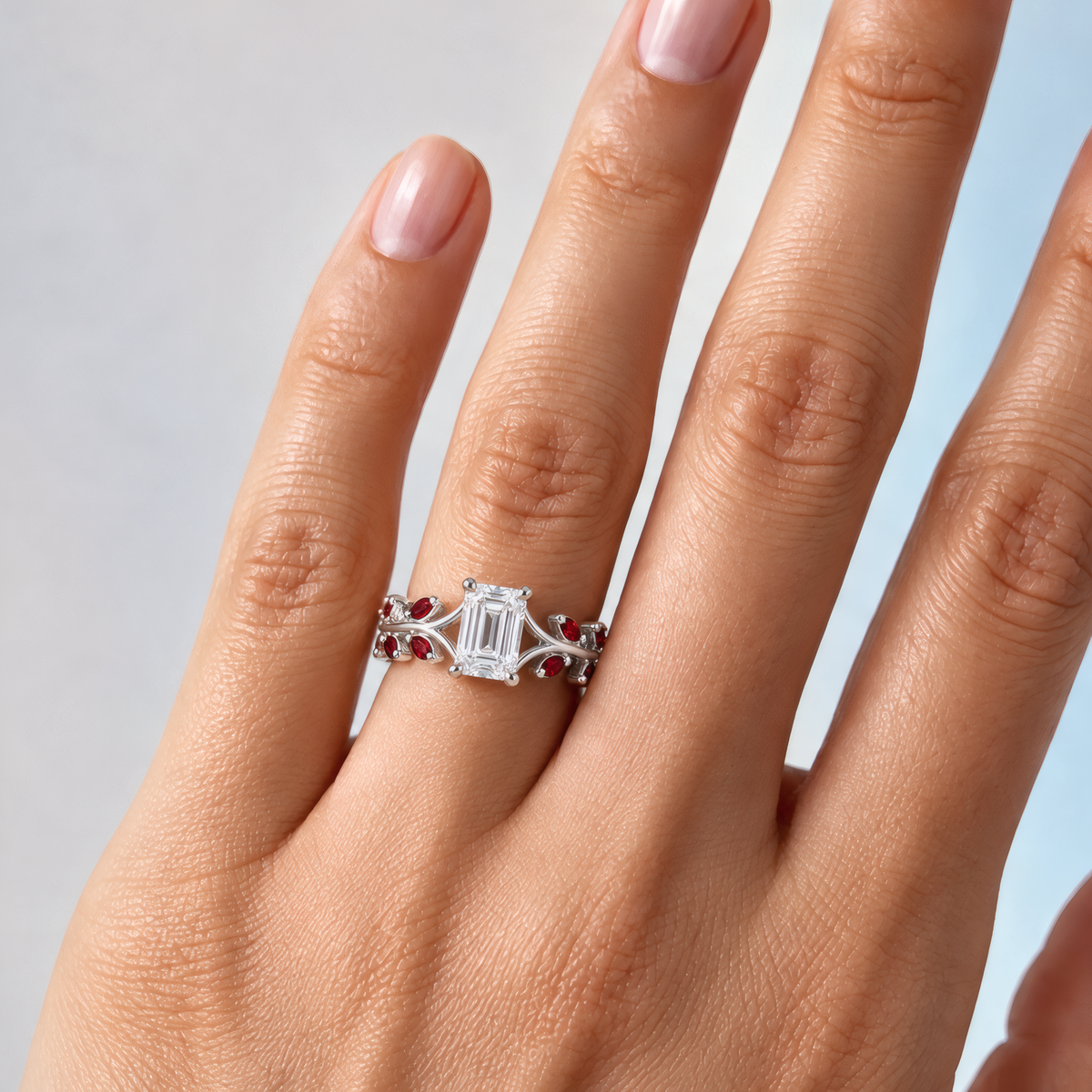Rosella engagement ring in white gold worn on a woman's hand, showing the emerald-cut diamond on an open vine band with ruby marquise leaves