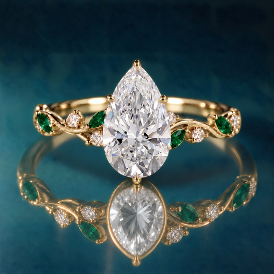 Gold engagement ring with large pear-shaped center stone and delicate vines covered in marquise green emeralds and round diamonds