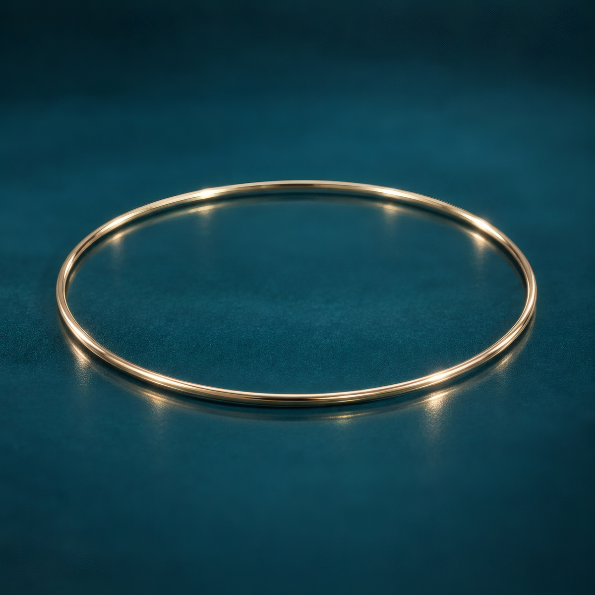 Slim 1.5mm 10k yellow gold bangle bracelet on a reflective teal surface.