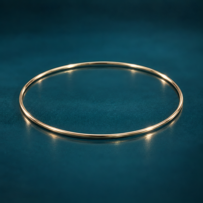 Slim 1.5mm 10k yellow gold bangle bracelet on a reflective teal surface.