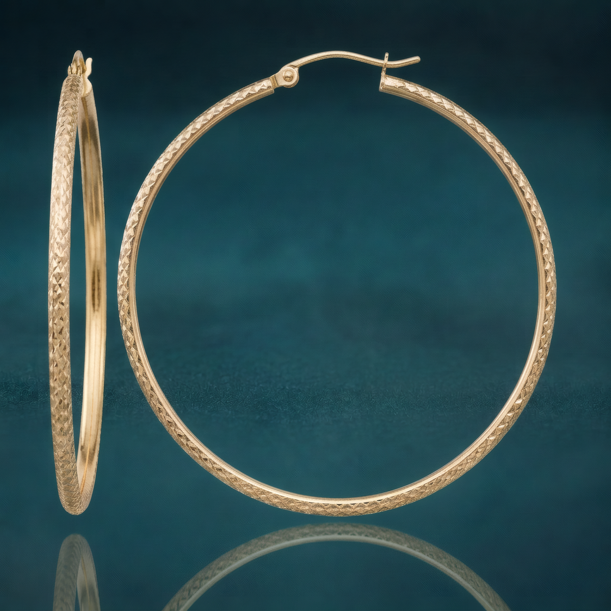 46mm 10k yellow gold hollow hoop earrings with an all-over diamond-cut texture, on a reflective teal surface.