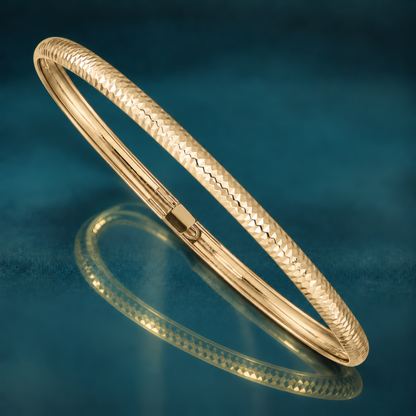4mm 10k yellow gold textured flexible bangle bracelet with a diamond-cut pattern, on a reflective teal surface.