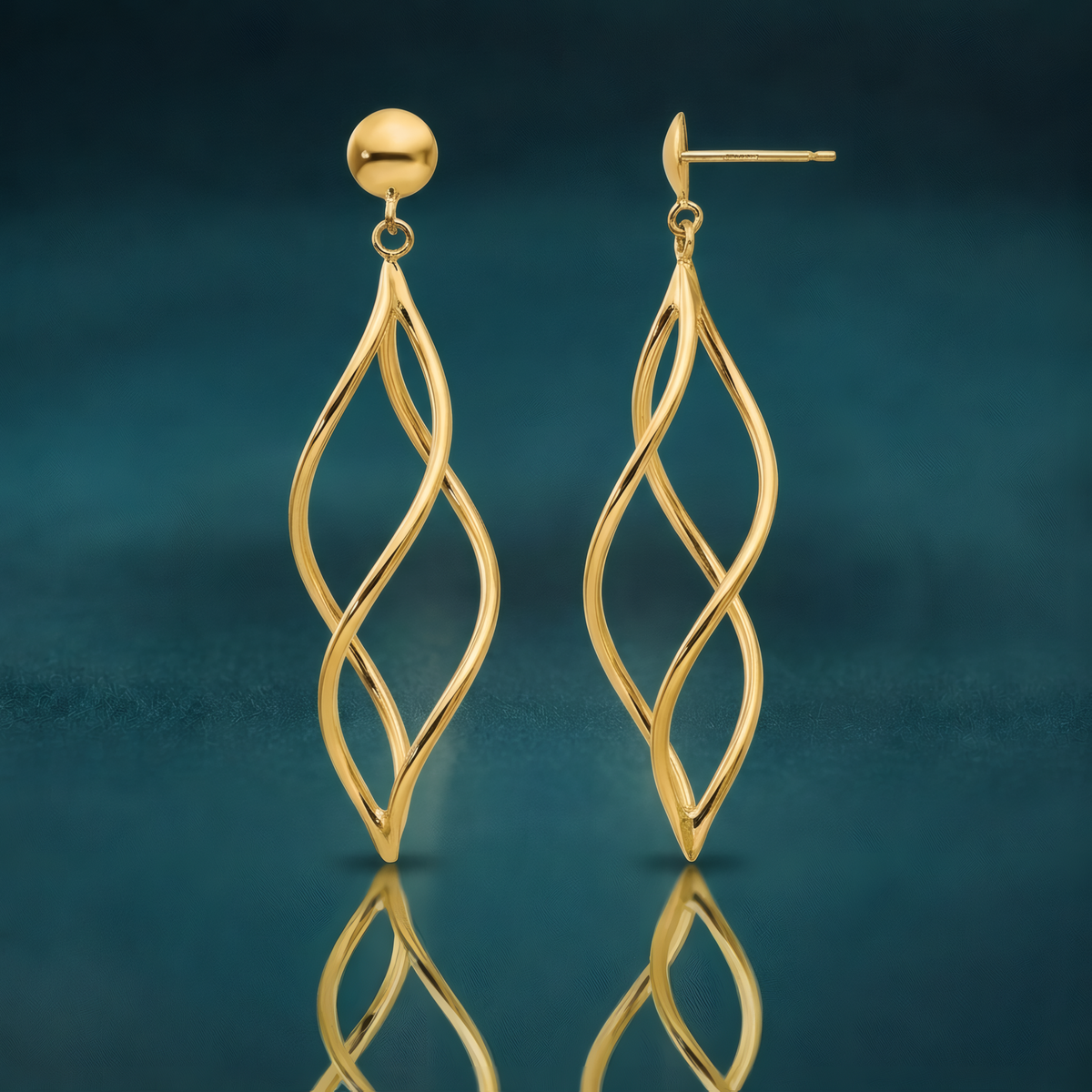 Long open twisted spiral dangle earrings in 10k yellow gold on ball posts, on a reflective teal surface.
