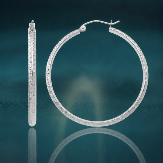 10k white gold hollow hoop earrings with an all-over diamond-cut texture, on a reflective teal surface.