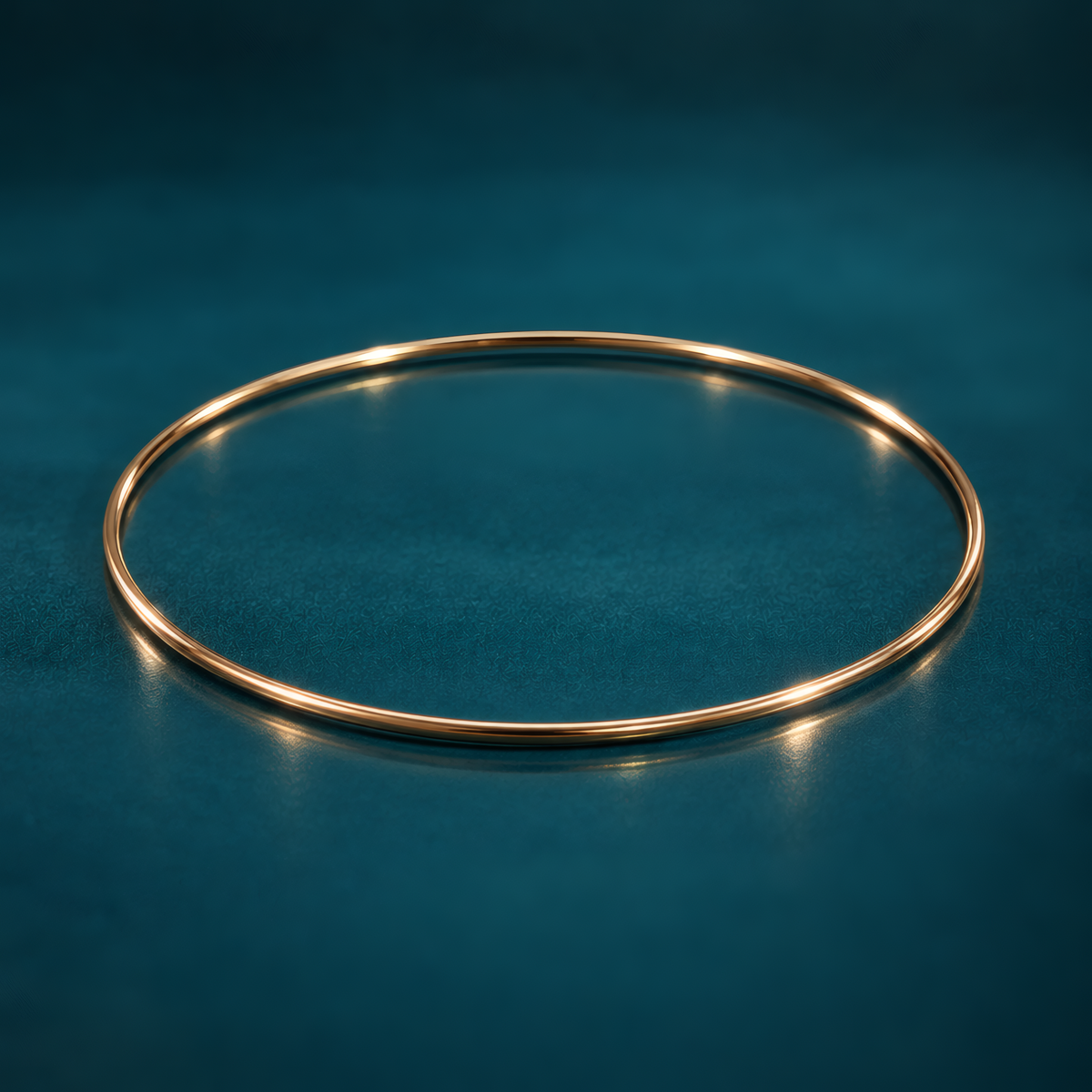 Slim 1.5mm 14k yellow gold bangle bracelet on a reflective teal surface.