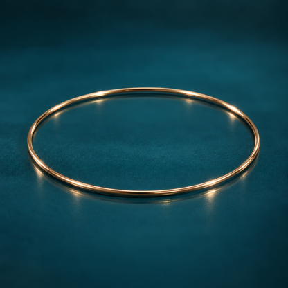 Slim 1.5mm 14k yellow gold bangle bracelet on a reflective teal surface.