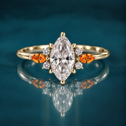 A gold engagement ring with a striking marquise center diamond, flanked on each side by a fiery amber marquise accent and a cluster of sparkling round diamonds that catch the light like autumn sun. A slender, polished band keeps the look delicate and refined.