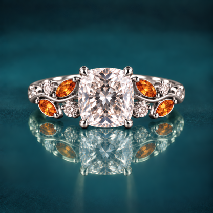 White gold engagement ring with a cushion-cut diamond atop a delicate vine band, woven with fiery amber marquise leaves and twinkling round diamonds for a romantic, nature-inspired look.