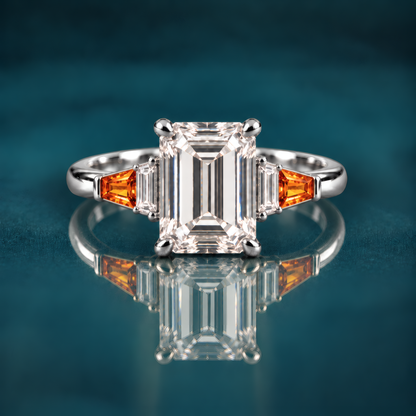 White gold engagement ring with emerald-cut diamond set in four classic prongs, framed by tapered amber baguettes and crisp diamond side stones that step down gracefully to a polished band.