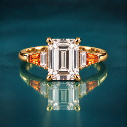 Gold engagement ring with emerald-cut diamond set in four classic prongs, framed by tapered amber baguettes and crisp diamond side stones that step down gracefully to a polished band.
