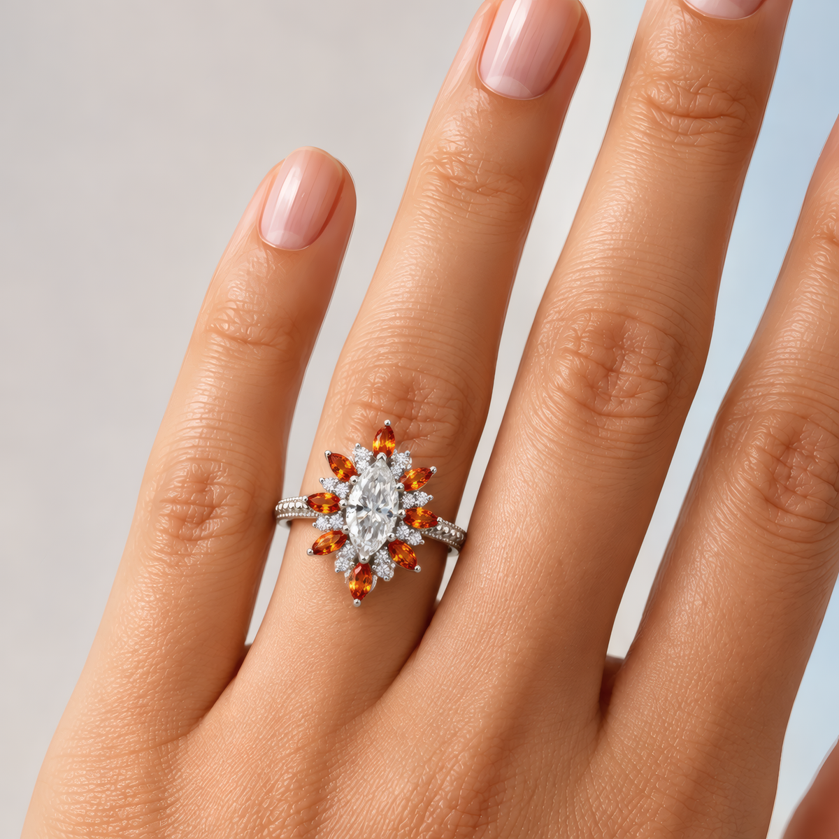 Ella engagement ring in white gold worn on a woman's hand, showing the marquise diamond in a sunburst halo of amber marquise stones