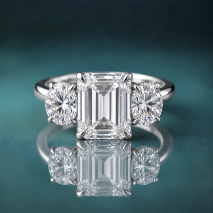 A white gold three-stone diamond ring featuring a central emerald-cut diamond flanked by two round-cut diamonds.