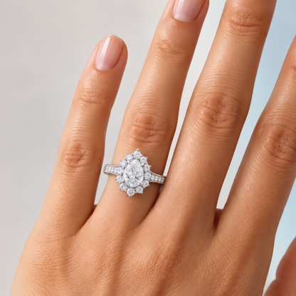 Delicate woman's left hand wearing a pear-shaped diamond halo engagement ring on the ring finger