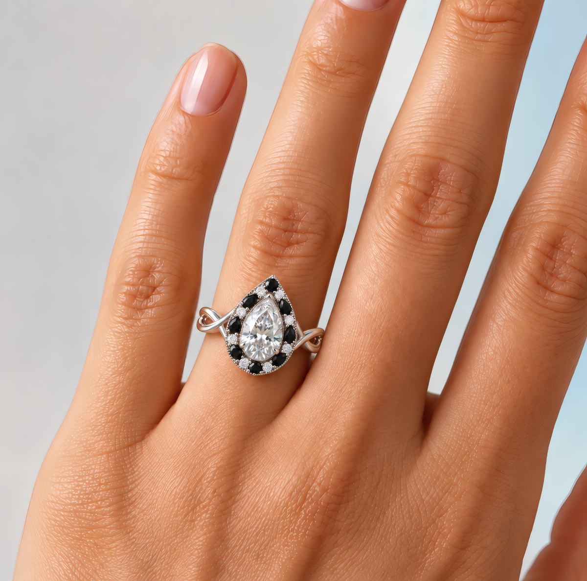 Kai engagement ring in white gold worn on a woman's hand, showing the pear-shaped diamond in a halo of black pear-shaped stones on a twisted band
