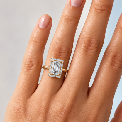 unique gold halo engagement ring with a baguette center diamond and a halo of baguettes and round diamonds. Worn on the left ring finger of a delicate woman's hand.