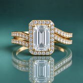 Gold halo engagement ring with an emerald-shaped center diamond and a curving double shank set with small diamonds.