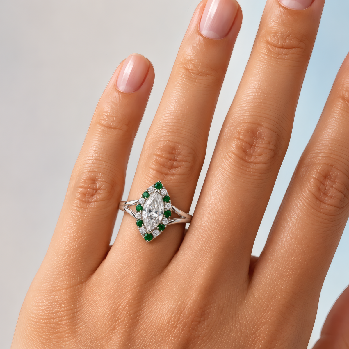 Lori engagement ring in white gold worn on a woman's hand, showing the marquise diamond in a green stone halo on a split-shank band