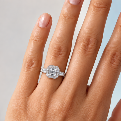 Delicate woman's left hand with a unique white gold halo three-stone engagement ring with an asscher-shaped center diamond adorning her ring finger.