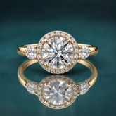 Gold halo three-stone engagement ring with a round center diamond and 2 pear-shaped side diamonds.