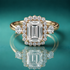 Gold halo three-stone engagement ring with an emerald-shaped center diamond and two large round shaped stones on the sides of the halo.