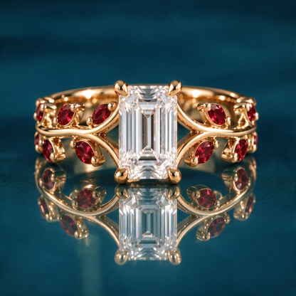 Rosella engagement ring in yellow gold with an emerald-cut diamond in four claw prongs on an open double vine band set with ruby marquise leaves and round ruby accents