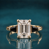 Tavi engagement ring in yellow gold featuring an emerald-cut diamond flanked by two tapered black baguettes
