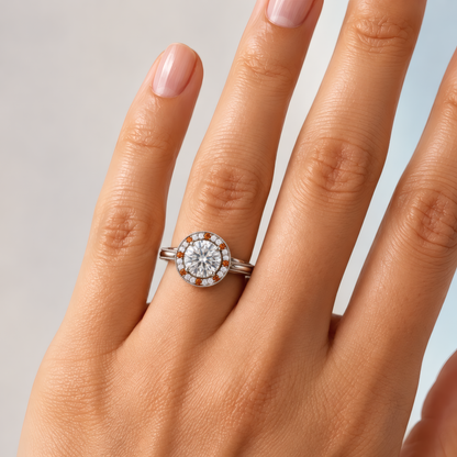 Tinga engagement ring in white gold worn on a woman's hand, showing the round brilliant diamond in a milgrain halo with cognac accents