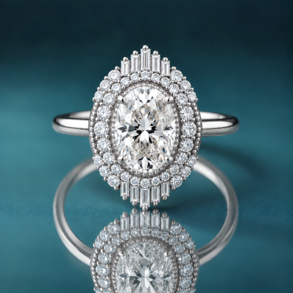 Unique white gold double halo engagement ring with an oval-shaped diamond in the center. Milgrain surrounds the center diamond, then a row of small tapering round diamonds, then another layer of round and baguette-shaped diamonds on the top and bottom of the inner halo. The shank is narrow and shiny.