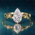 Gold engagement ring with  large pear-shaped center stone and delicate vines covered in marquise green emeralds and round diamonds
